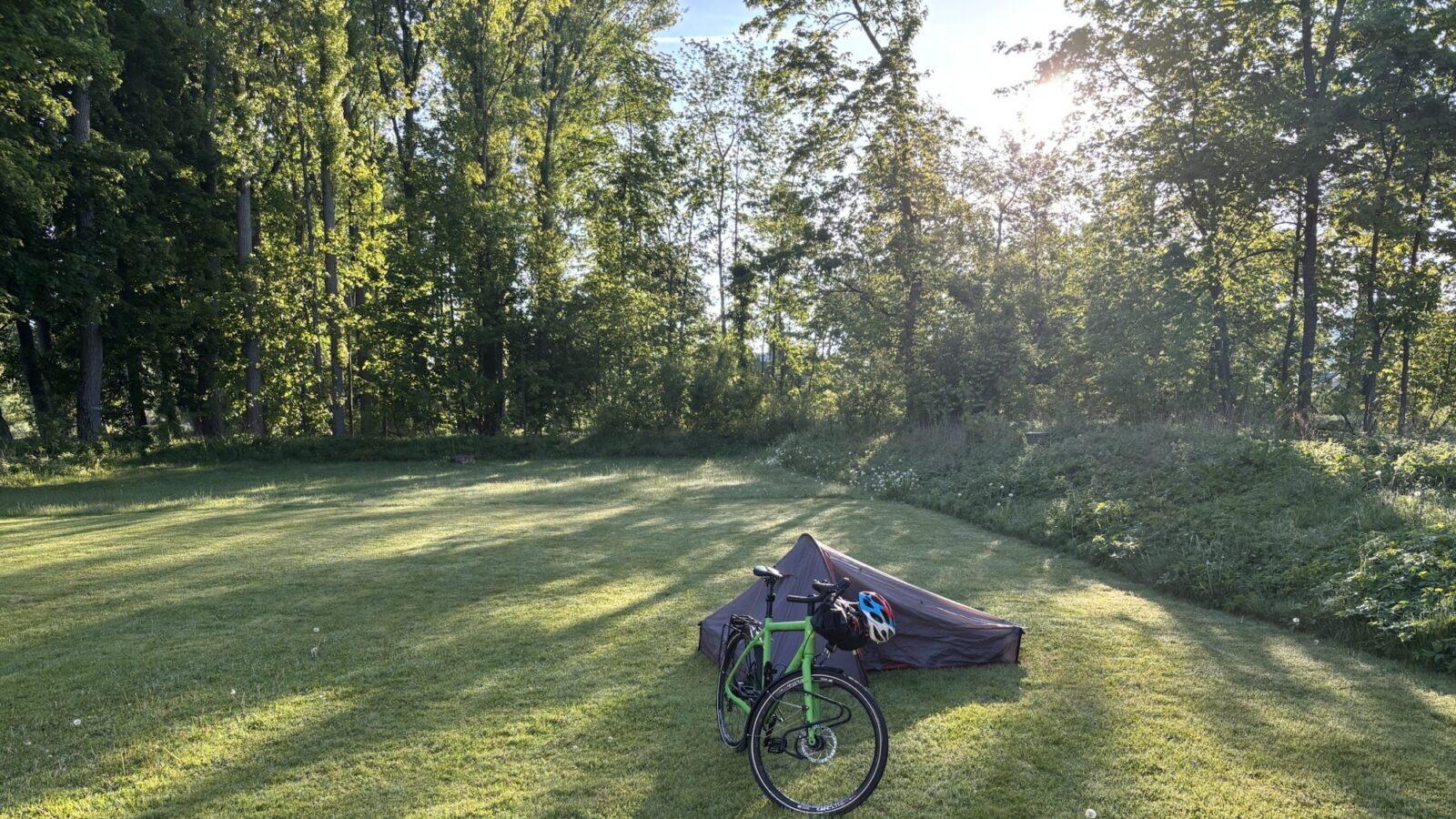A meadow in the sunrise, with a bicycle and a small tent