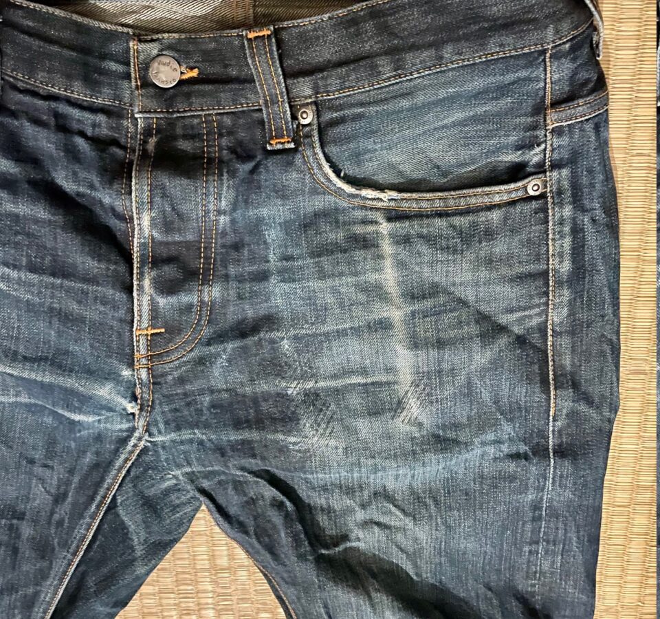 Close-up of the left pocket of a blue jeans. You can clearly see the contours of a smartphone in the coloring of the fabric.