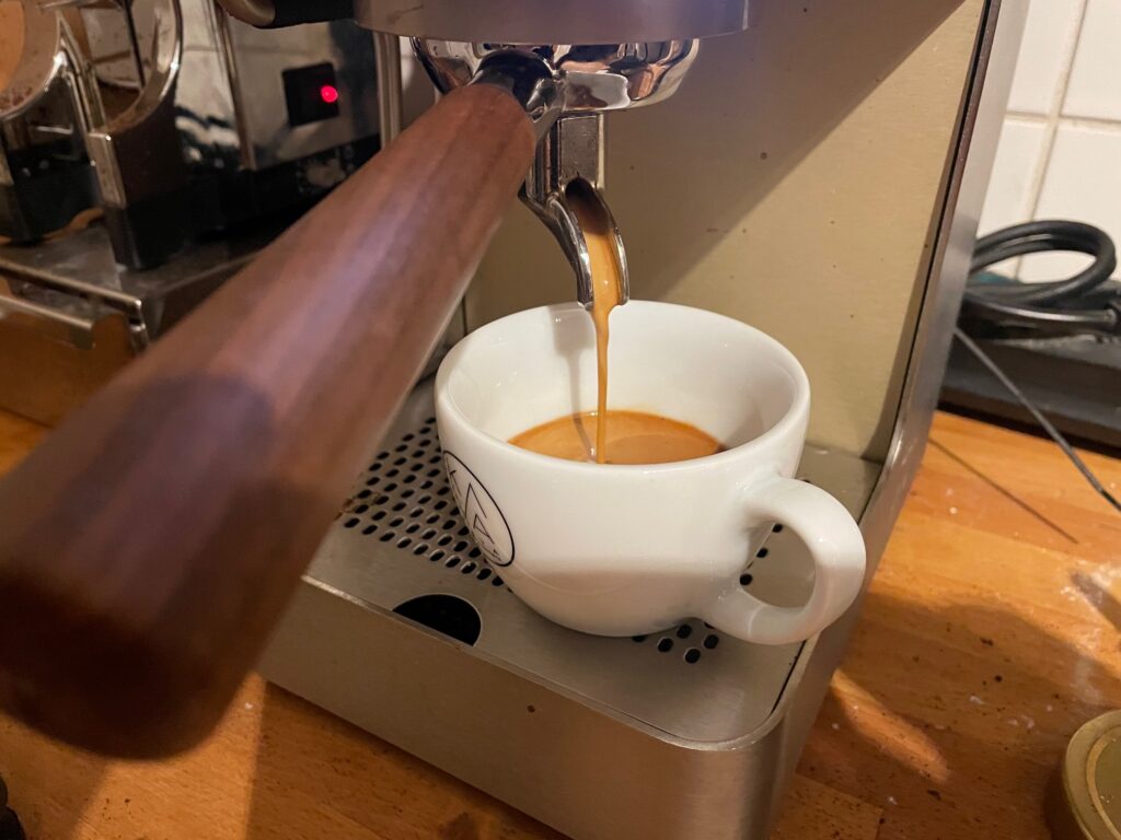 Close-up shot of the Zuriga machine making an espresso. The coffee is running into a white cup. It's light brown and creamy.